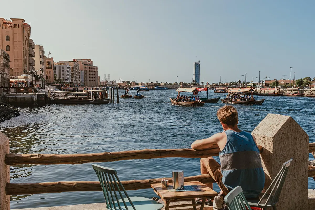 dubai creek, waterfront, man sitting, abra boats, traditional boats, dubai water taxis, relaxing view, outdoor seating, creek view, people, abra ride, sunny day
