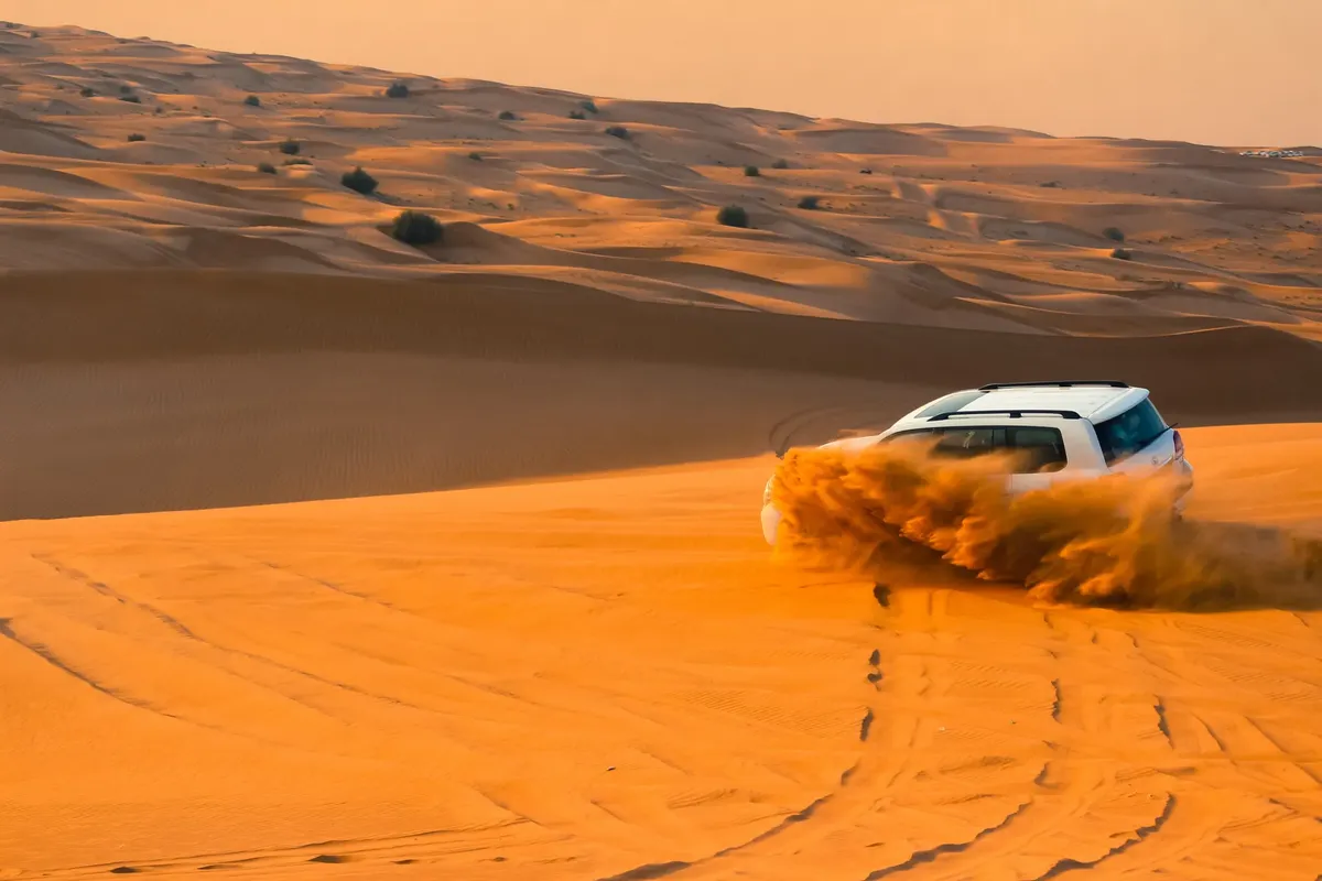 A thrilling SUV driving through the sand dunes of Dubai's desert landscape at sunset.
