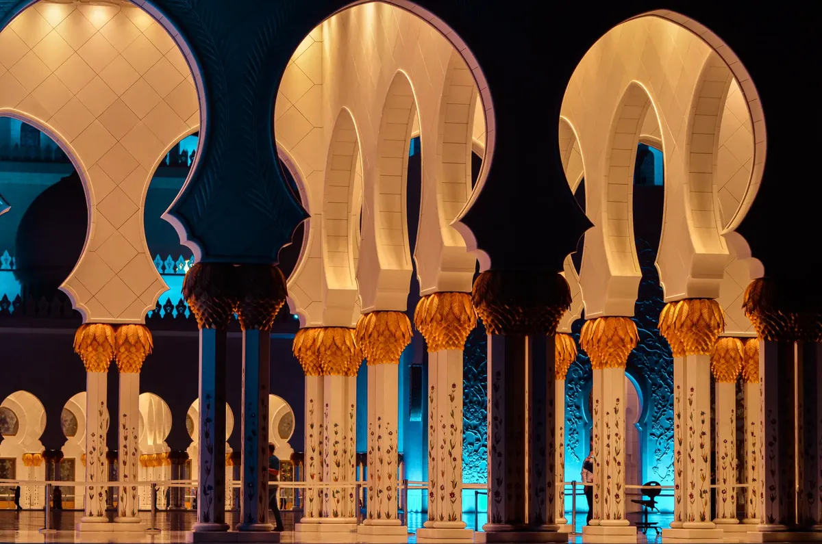 Intricate arches of Sheikh Zayed Grand Mosque in Abu Dhabi at night, beautifully lit with warm and cool tones.
