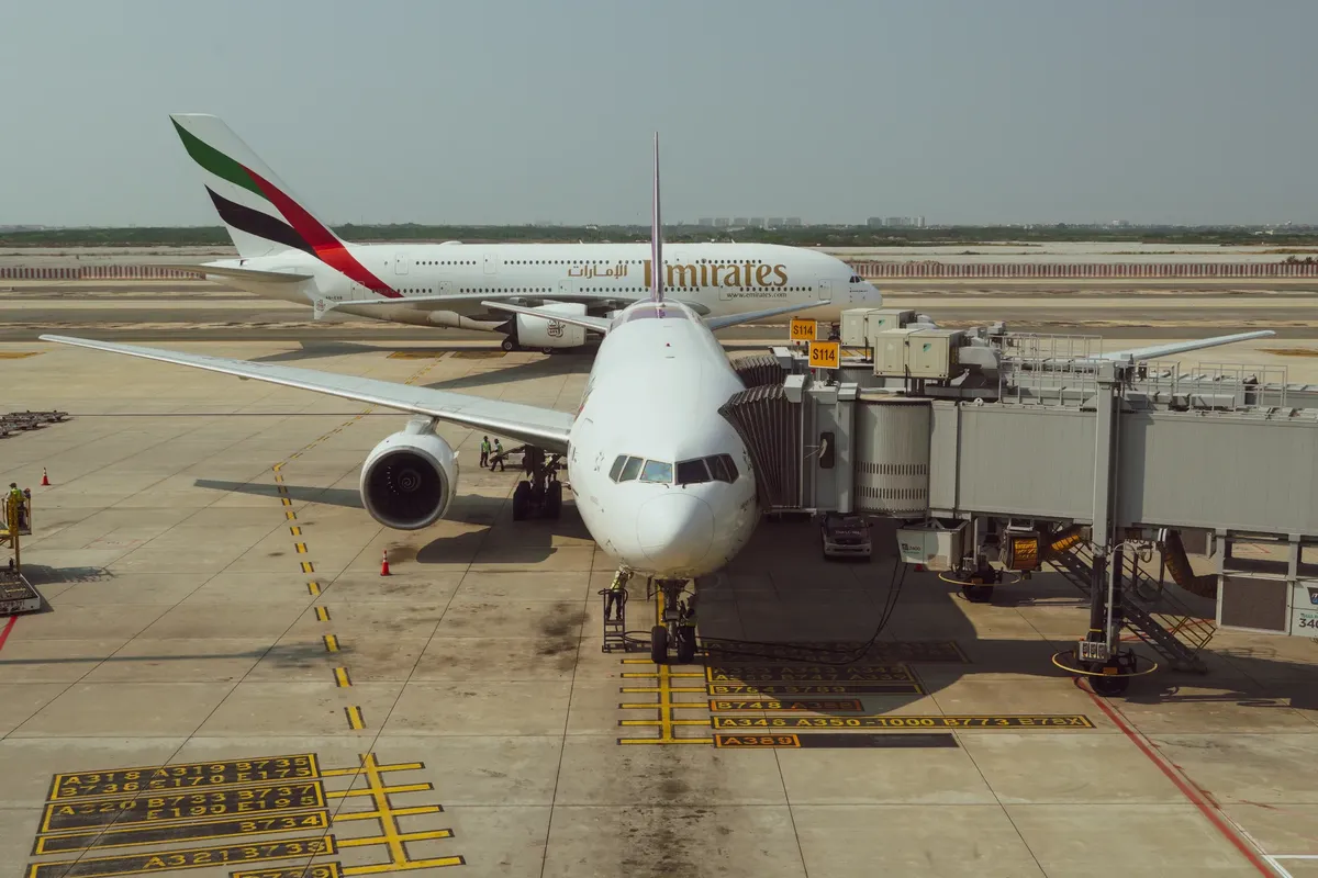 Passenger planes at an airport terminal with clear skies and visible jetway.